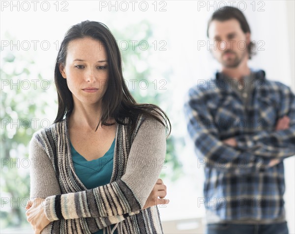 Sad woman with arms crossed, man in background.