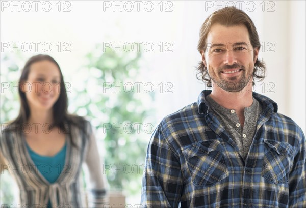 Smiling man looking at camera, woman in background.