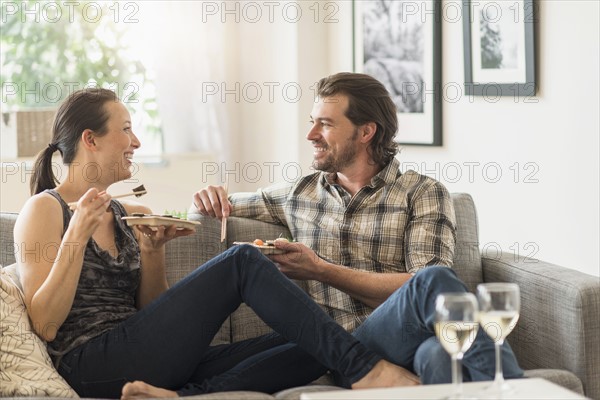 Cheerful couple eating on sofa.