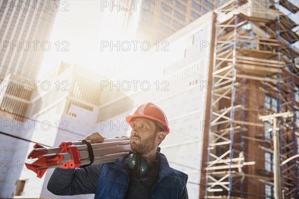 Construction worker carrying tripod on shoulder.