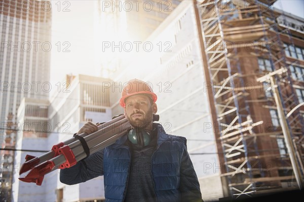 Construction worker carrying tripod on shoulder.