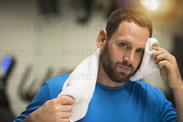 Portrait of tired man wiping face with towel.