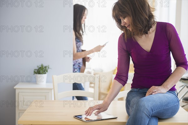 Teenage girl (14-15) texting and mom using digital tablet in living room