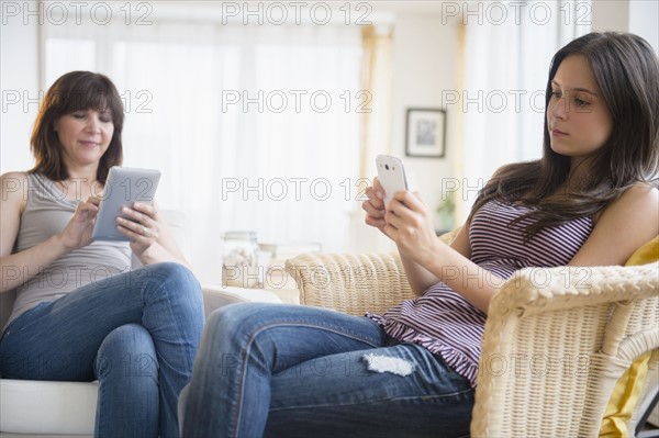 Teenage girl (14-15) using smart phone and mom using digital tablet in living room