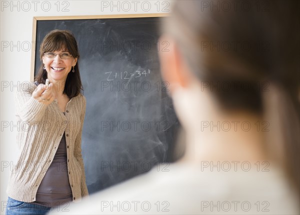 Teacher encouraging teenage student (14-15) to come to blackboard