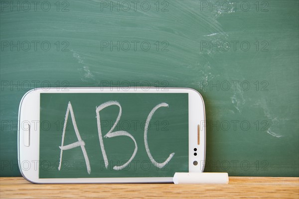 Smartphone leaning against chalkboard with ABC letters displayed