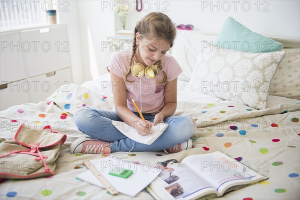 Girl (12-13) sitting on bed doing homework