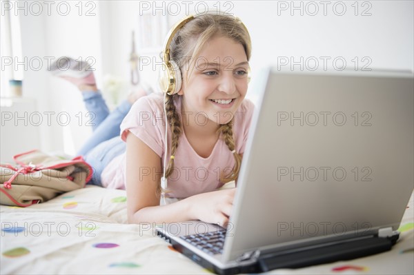 Girl (12-13) lying in bed using laptop