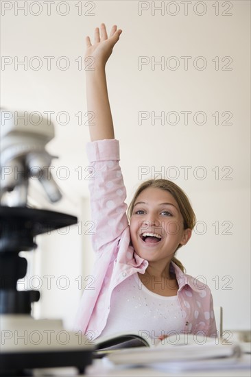 Girl (12-13) raising hand to answer question at school