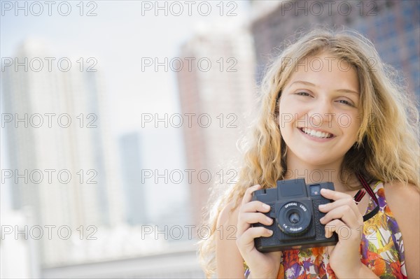 Girl (12-13) holding camera, smiling