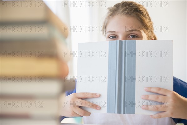 Teenage girl (12-13) hiding face behind book