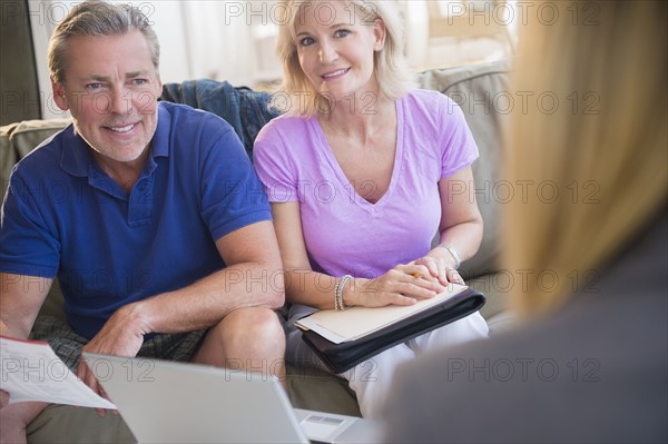 Portrait of couple sitting on sofa smiling at woman in blurred foreground