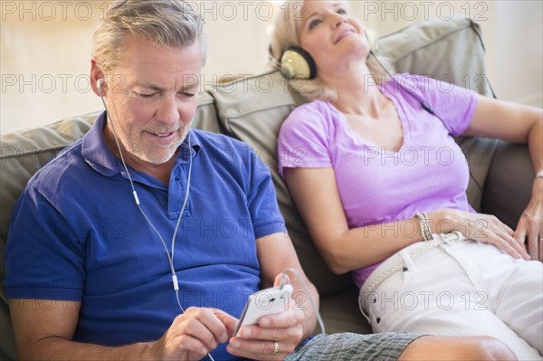 Portrait of couple sitting on sofa listening to music on headphones