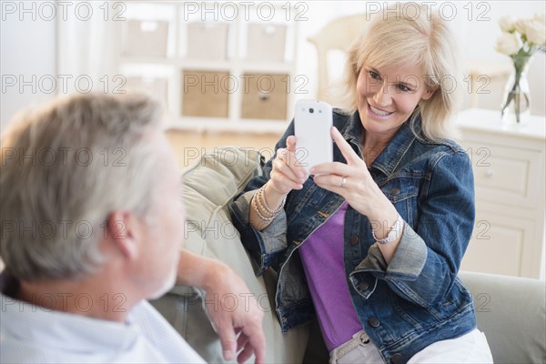 Portrait of woman photographing man with smartphone, sitting on sofa