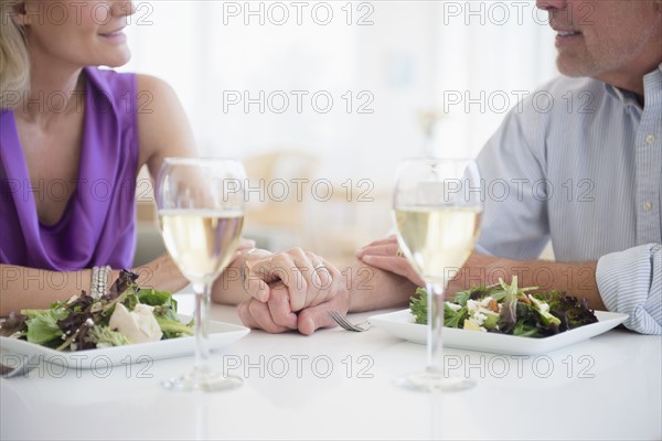 Cropped view of couple holding hands in restaurant with glasses of white wine in foreground