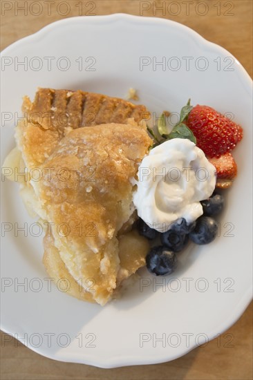 Close-up shot of portion of apple pie with fresh berries and cream on white plate