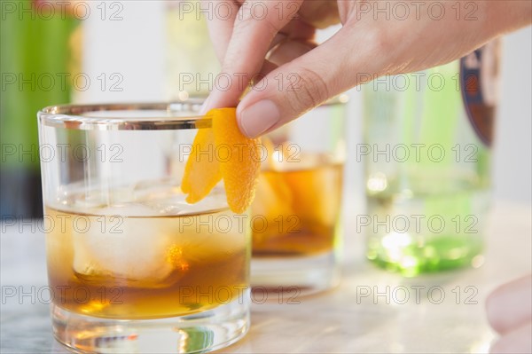 Close-up shot of bartender's hand decorating cocktail glass with orange peel
