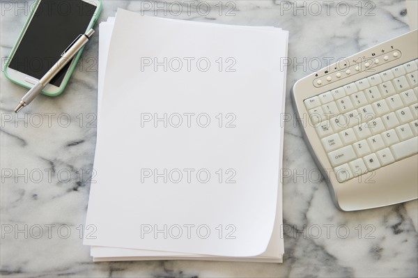 Studio shot of smart phone, sheets of paper, pen and computer keyboard