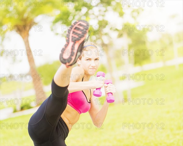 Young woman exercising in park using dumbbells