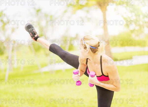 Young woman exercising in park using dumbbells