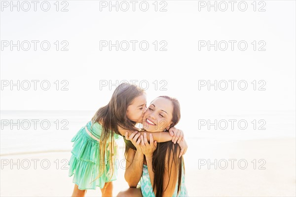 Girl (6-7) kissing her mother on cheek on beach