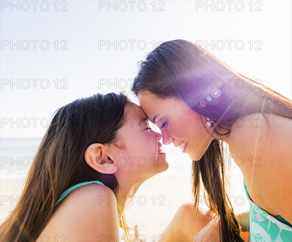 Mom and daughter (6-7) rubbing noses on sunny day on beach
