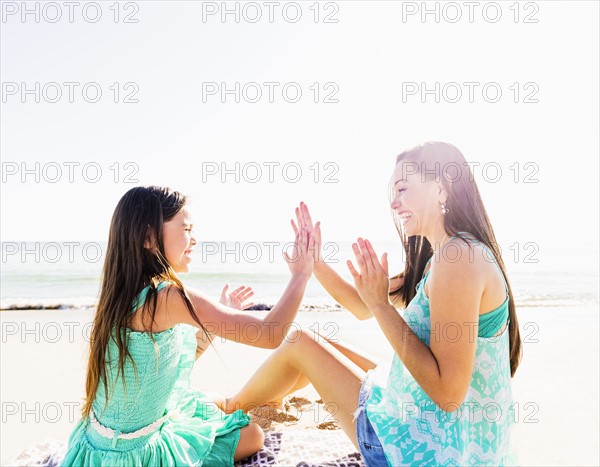 Mom and daughter (6-7) playing patty cake on beach