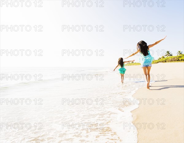 Rear view of girl (6-7) and her mom running on beach