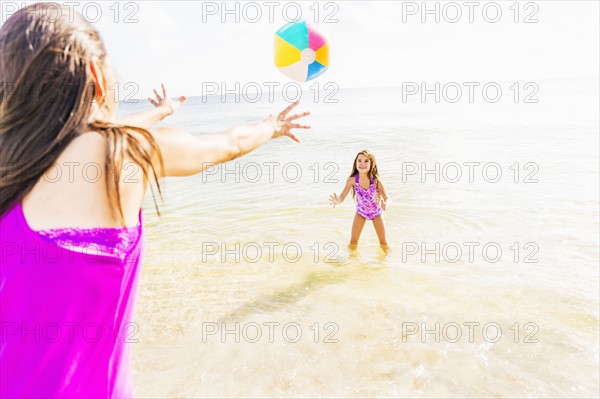 Mom throwing beach ball to her daughter (6-7) on beach