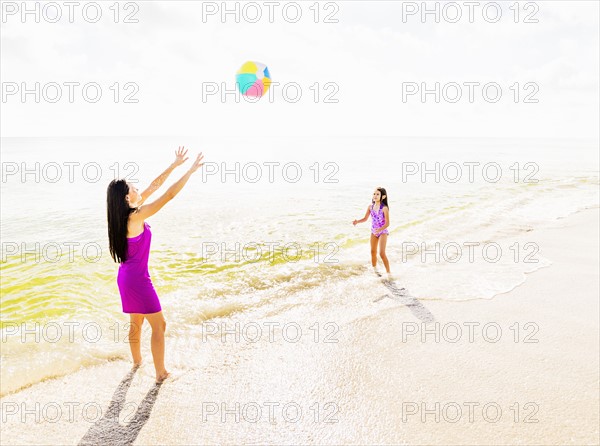 Mom throwing beach ball to her daughter (6-7) on beach