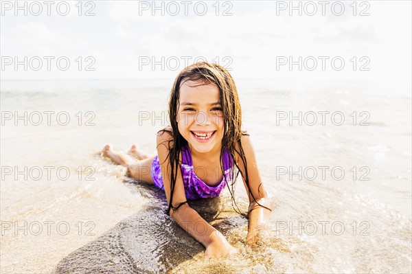 Portrait of girl (6-7) lying in sand on beach