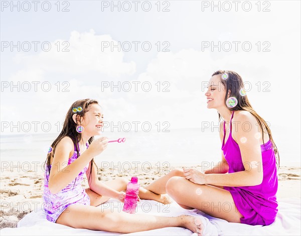 Mom and her daughter (6-7) sitting on blanket on beach