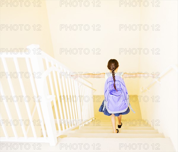 Girl (6-7) with backpack walking down stairs at home
