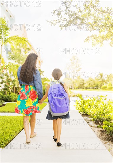 Rear view of girl (6-7) holding hands with her mom outdoors