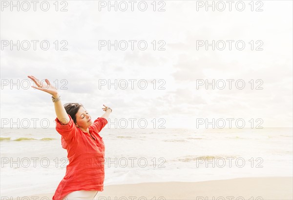 Side view of woman standing with arms up on beach