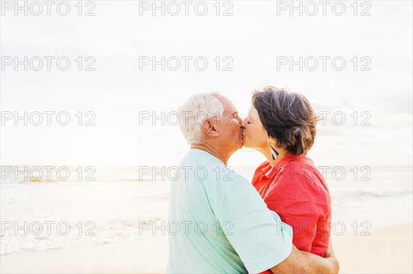 Older couple kissing on beach at sunrise