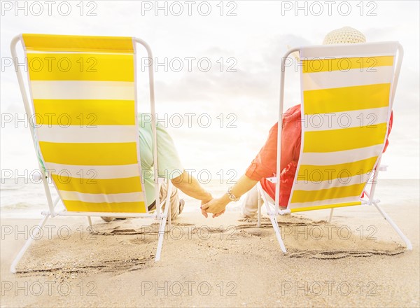 Rear view of couple sitting in lounge chairs on beach