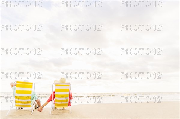 Rear view of couple sitting in lounge chairs on beach