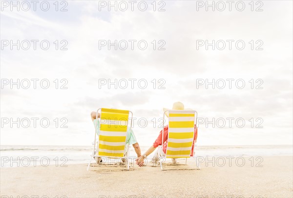 Rear view of couple sitting in lounge chairs on beach