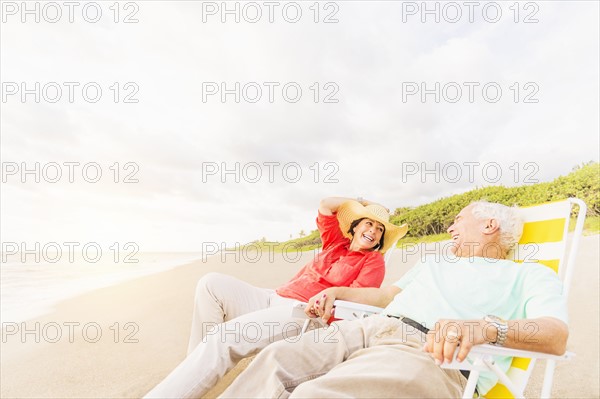 View of couple sitting in lounge chairs on beach and laughing