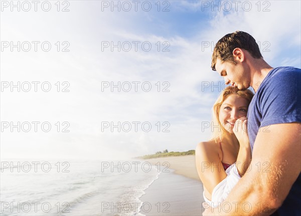 Portrait of young couple embracing on sandy beach, against background of coastline