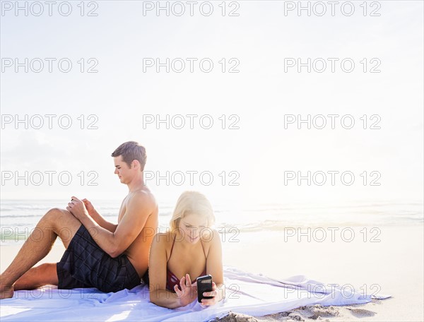 Portrait of young couple relaxing on beach, using smart phones