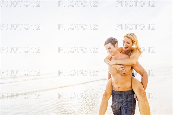 Boyfriend carrying girlfriend piggyback on beach