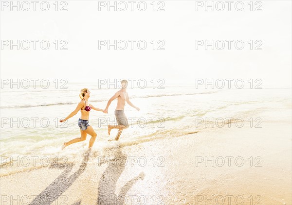 Young couple running in surf holding hands