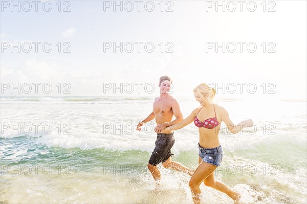 Young couple running in surf holding hands