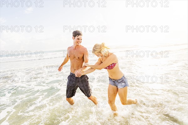 Young couple running in surf holding hands