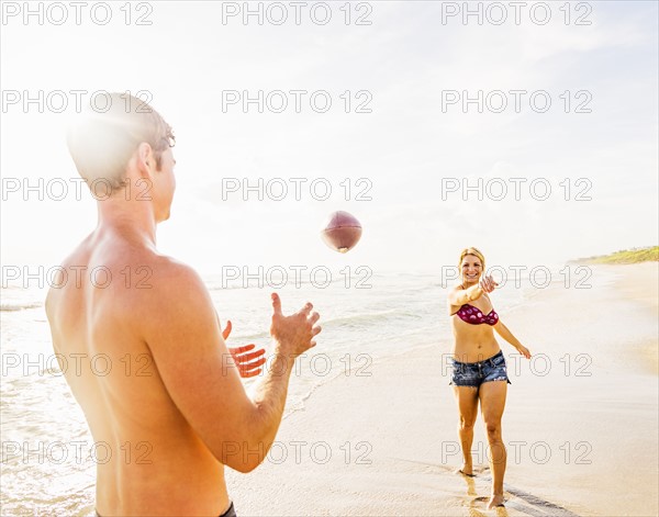 Young couple throwing football on beach