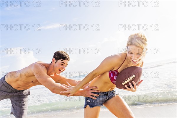 Cheerful young couple playing football on beach