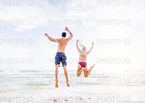 Rear view of young couple jumping on beach