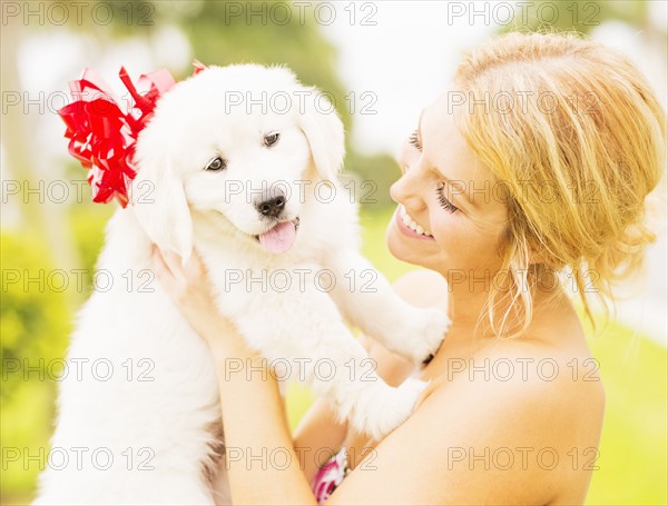 Young woman holding white puppy with ribbon bow